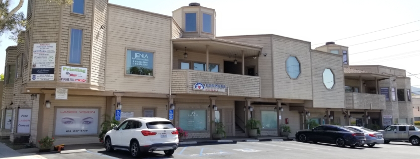 Two-story beige commercial plaza with parked cars