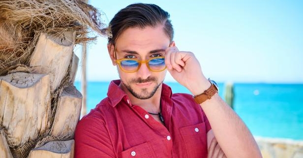 Young man adjusting sunglasses by palm tree