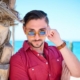 Young man adjusting sunglasses by palm tree