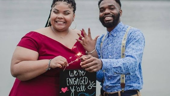 Happy couple showing engagement ring and sign