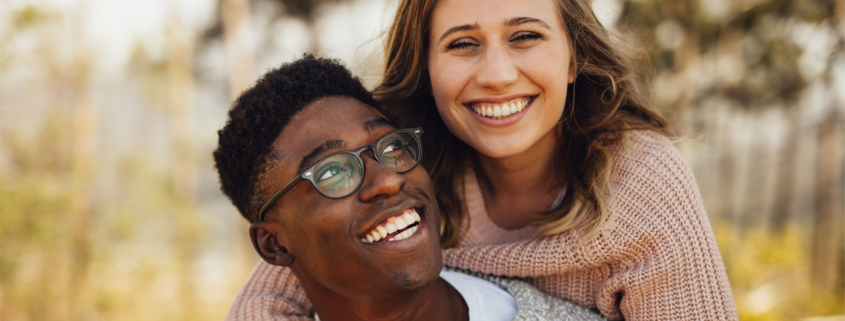 Smiling interracial couple outdoors, woman hugging man