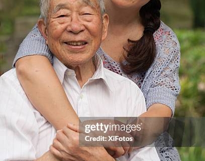 Woman hugging elderly man, both smiling outdoors