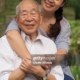 Woman hugging elderly man, both smiling outdoors