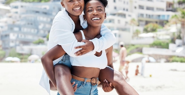 Two women laughing, piggyback on sunny beach