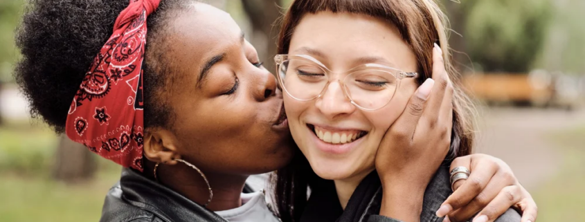 Woman kissing friend on cheek in park