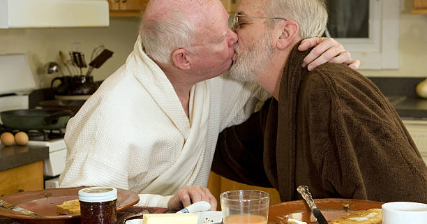 Two older men kissing at breakfast table