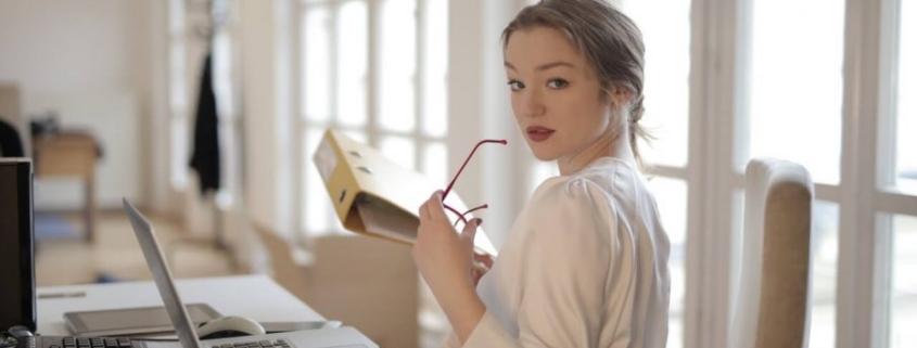 Woman holding glasses at desk, looking back