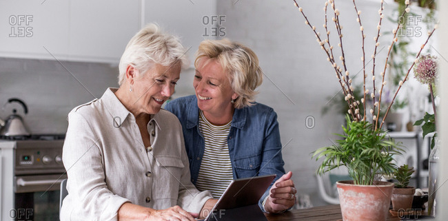 Two senior women using tablet in kitchen